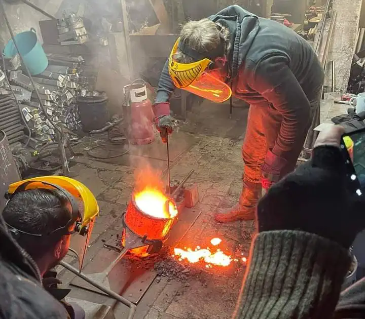 Two workers in a foundry pouring molten Brass, with protective gear.