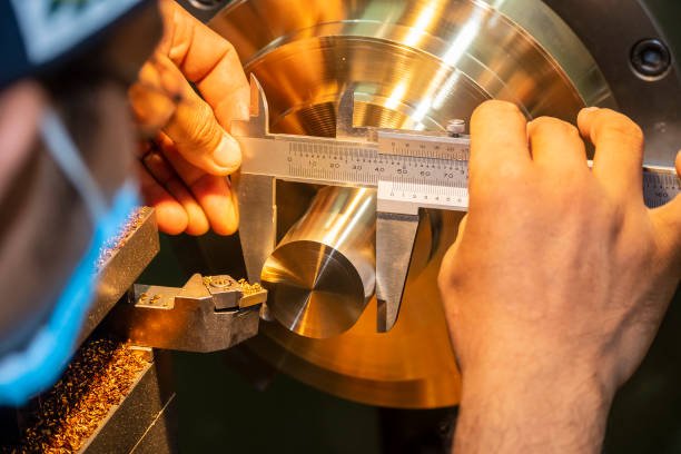 Person measuring a metallic part with a caliper on a lathe machine.