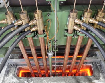 Industrial machinery with glowing hot metal and several hydraulic pipes.